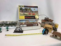 Photo showing loose buildings, model trees, black bridge piece, measuring tape and boxed kits for water tower and feed station
