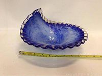 Blue and white art glass wave bowl with clear, scalloped edge shown with measuring tape for size reference, approximately 10 inches.