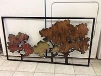 Full view of large metal wall art with three tree silhouettes, framed in black metal, showing rust-colored, reddish, and greenish patina.