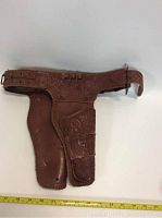 Full view of the brown toy holster showing size against ruler, embossed decoration, and shape including belt strap and ammo loops