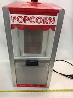 Front view of Dolce popcorn machine featuring clear panels, red top with ventilation slots, and control panel at bottom front.