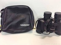 Photo showing black zippered carrying case with white 'tasco' branding and Tasco binoculars positioned next to it.