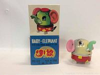 Toy and box together showing baby elephant tin toy and original packaging front view with colorful graphics and Chinese text.