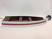 Side view of small wooden rowboat model showing white exterior with red stripe and three cross seats inside. Measures about 19.5 inches in length.