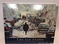 Front cover of 'The Ice Storm' book showing a snow-covered street with fallen tree branches and cars, with a walking figure carrying plastic bags.