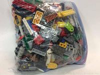 Large sealed transparent plastic bag filled with assorted LEGO pieces of different colors and shapes including bricks and wheels.