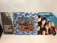 Three Rolling Stones LP records standing upright showing front covers: December's Children, colorful multi-figure artwork album, Through the Past Darkly.