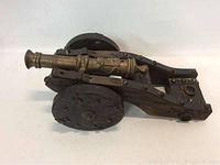 Side angled view of solid brass model cannon mounted on dark stained wooden carriage with large wheels and metal rivets.