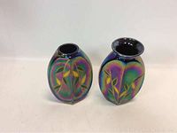 Both blue iridescent glass vases with foliage design photographed side by side