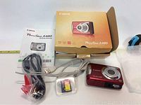 Canon PowerShot A480 camera, original box, instruction manual, USB cable, AV cable, SD card, and wrist strap all displayed.