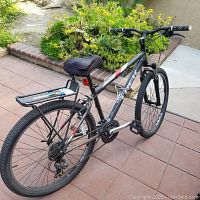 Full side view of the Trek mountain bike showing black frame with red and white decals, rear rack, seat, pedals, knobby tires.