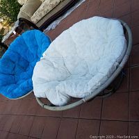 Two circular hoop chairs with thick fluffy cushions—one blue and one white—shown outdoor on tiled floor; visible wear and damage to one chair frame.