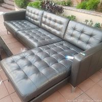 Front view of the L-shaped black leather sofa with tufted cushions and chaise end.