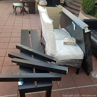 Dining table parts including legs, table top sections, and two white fabric chairs wrapped in protective plastic