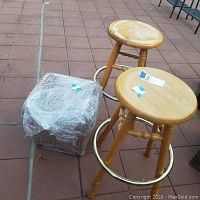Two wooden barstools and wrapped wicker ottoman on tiled floor outdoors