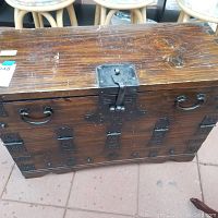 Front view of vintage wooden chest showing metal handles and decorative black metal hardware on front and corners.