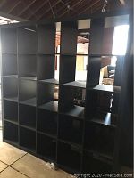 Front and side views of large black shelving unit showing 25 square cubby holes in a 5x5 formation. Visible wear on surfaces. Shelving unit is large and heavy.