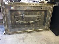 Full view of ornate shadow box displaying sword and sheath on grey backing