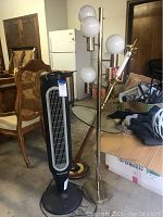Full view of Honeywell fan, 5-bulb metal floor lamp, and floor lamp with embedded glass table in a garage setting.