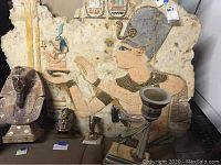 Wide shot showing the large Egyptian wall art panel with detailed painted figure, accompanied by three busts (two King Tutankhamen and one Nefertiti) and a decorative candle holder.