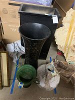Photo showing all four items in the lot including the black wood planter, textured metal vase, green ceramic planter, and white ceramic vase with desert motif.