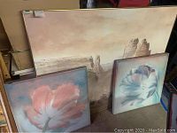 Three paintings grouped together: one large desert landscape and two smaller floral paintings with flowers on blue-green backgrounds.