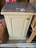 Front view of wood cabinet with single paneled door and metal knob, topped with a brown and beige veined marble slab.