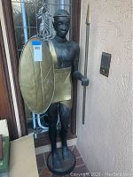 Full front view of metal sentry statue showing overall posture, shield and spear