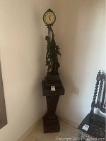 Full view of the clock statue atop the wooden pedestal in a corner.