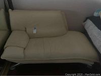 Full view of tan leather chaise lounge positioned against a wall with a tan leather pillow on it.