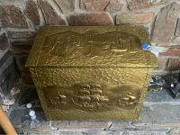 Front view of the chest showcasing the metal repoussé overlay with sailing ship scenes and textured metal background.