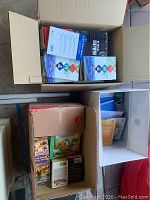 View of an open box containing multiple books in English and Korean, showing colorful book covers and some visible marks and stains.