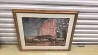 Photo of framed lithograph showing a building surrounded by trees, signed by Kubik.