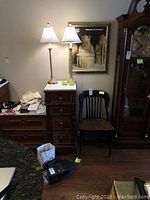 Wide view of the corner with the pair of candlestick lamps on a wooden chest and the vintage wooden school chair next to them.