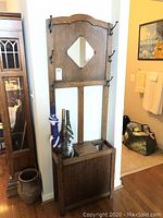 Front view of antique English oak hall tree showing diamond-shaped mirror, eight coat hooks, and umbrella stand with three umbrellas inside.