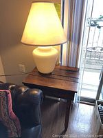 White glass table lamp lit on top of the English school desk beside a leather armchair and sliding glass door.