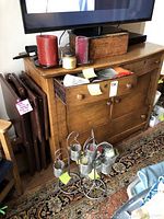 Candles including large red and purple pillar candles, small jar candle on a wooden cabinet, with two metal mesh handmade standing candle holders on floor in front.
