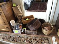 Wide view showing assorted vases, glass jar with corks, and various wicker baskets arranged on floor near wooden dresser.