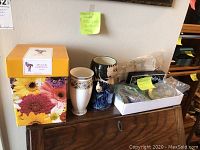 Lot of vases and miscellaneous items on wooden shelf, including boxed yellow-floral Vis A Vis Formfindung vase, pink Ritzenhoff lady vase, white floral Wedgewood vase, and plastic container with miscellaneous hardware items