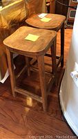 Two wooden pub stools showing natural wood grain and condition, one seat with a wood split.