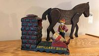 Photo showing vintage cast iron artillery bank with soldier figure and wooden horse in background