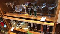 Full shelf view of assorted glassware including colorful stem Ritzenhoff glasses, clear martinis, and candle holders