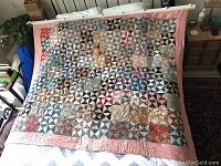 Vintage American quilt laid across a bed, showing overall pattern and colors with wooden rod placed on top for hanging.
