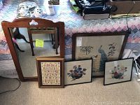 Photo showing the Willett wood-framed wall mirror with decorative top cut-out, and four framed embroidery pieces leaning against the bed.
