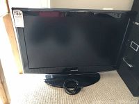 Front view of Samsung 32 inch TV with stand and power cord coiled on base, no remote visible.