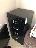 Front angle view of black two-drawer metal filing cabinet showing handles and label holders.