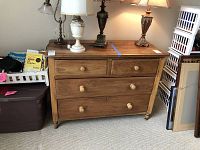 Front view of wooden dresser with four drawers and four turned legs, displaying two smaller drawers on top and two larger drawers below. Lamps and books are on and around the dresser.
