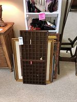 Wooden knickknack shelf with multiple compartments standing vertically with a white tag, four framed posters stacked behind it.