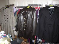Photo of three men's coats on rack: gray wool, brown vinyl with gold buttons, and black wool double-breasted.
