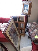 Two mirrors leaning against wall, one framed print standing on the floor, and wooden art display stand holding a framed print upright